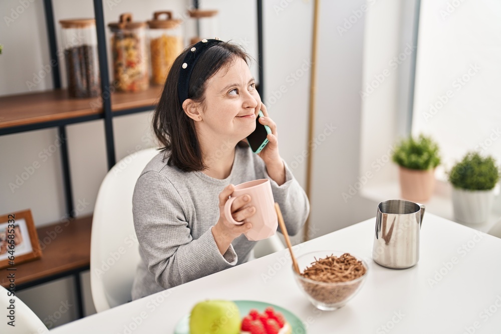 A young woman on the phone at her kitchen table, with a cup of tea